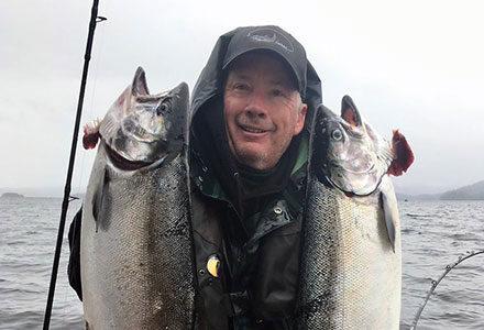 Guest holds up two king salmon on a fishing boat.
