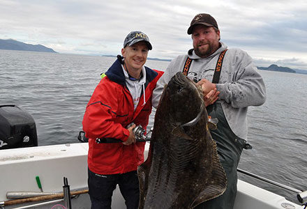 Two guest struggle to hold a large halibut just caught on the fishing boat.