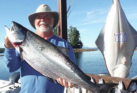 Guest holds his kind salmon catch with a 121 pound halibut hanging in the background.