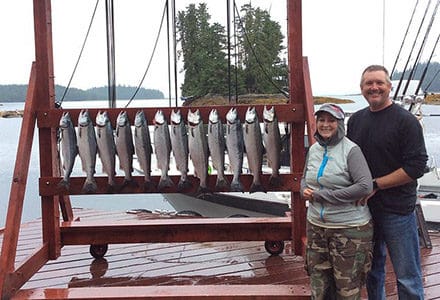 Guest stand next to their silver salmon catch displayed on the lodge sign.