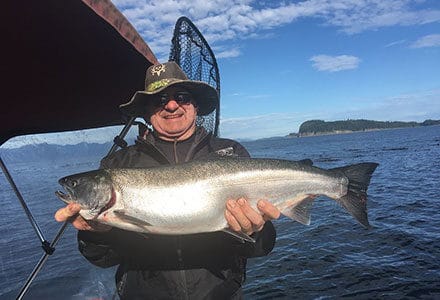 Guest holds king salmon on fishing boat.