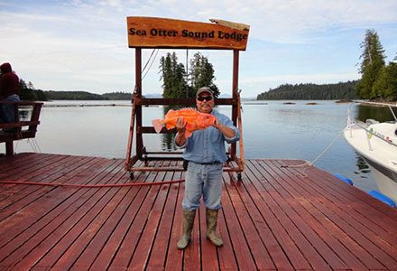 Guest poses in front of lodge sign with yelloweye rockfish.