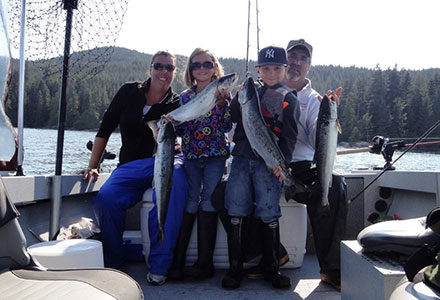 Family of four pose on a fishing boat with their salmon catch.