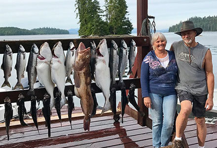 Guest couple poses with their catch hanging on the lodge sign including a large ling cod.