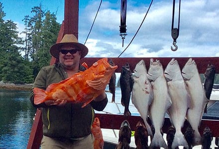 Guest holds a yelloweye rockfish next to the rest of his catch displayed on the lodge sign.