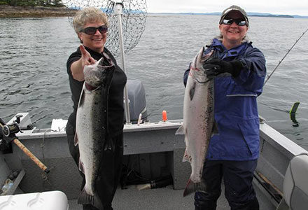 Two women guests smile big while holding their king salmon catch on the fishing boat.