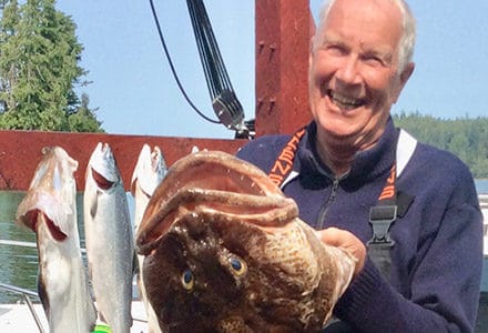 Guests holds a huge ling cod next to the rest of his catch displayed on the lodge sign.