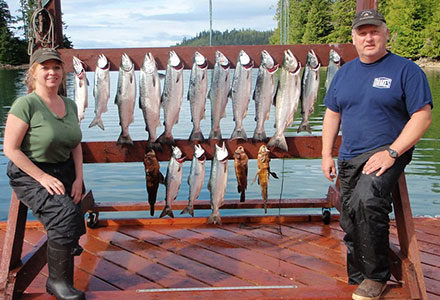 Guest couple show their nice salmon and rockfish catch on the lodge sign.