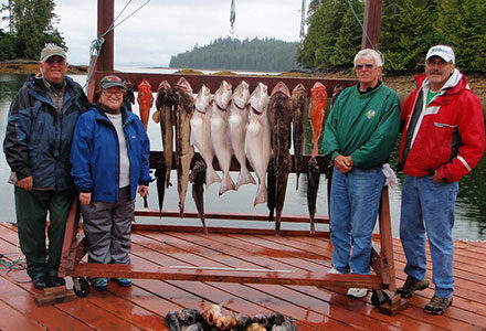 Four guests pose with their halibut, rockfish and ling cod catch hanging on the lodge sign.