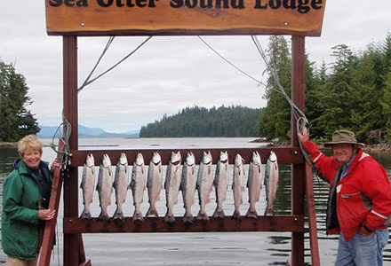 A guest couple pose with their salmon catch, lined up on the lodge sign.