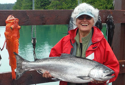 Woman holds a nice king salmon with a yelloweye rockfish hanging on the sign behind her.