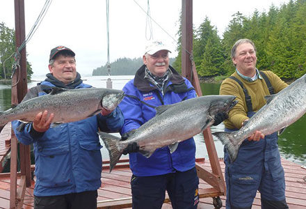 Three guests hold their impressive king salmons on the dock.
