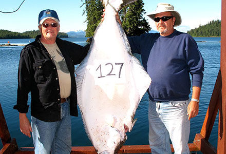 Two guests stand with their hanging 127 pound halibut catch.