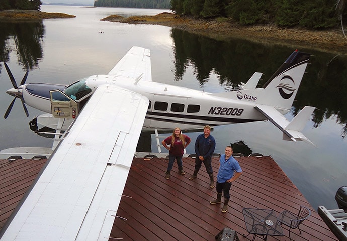 The crew poses next to a float plane on the dock after loading.